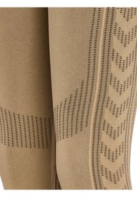 Gros plan sur un tissu beige avec des motifs perforés texturés verticaux et diagonaux sur un pantalon ou un legging.