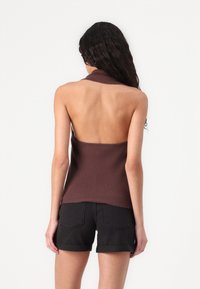 Rjav rebrast halter top z odprtim hrbtom, ki se prilega telesu in ima visok ovratnik. V kombinaciji z črnimi denim kratkimi hlačami.