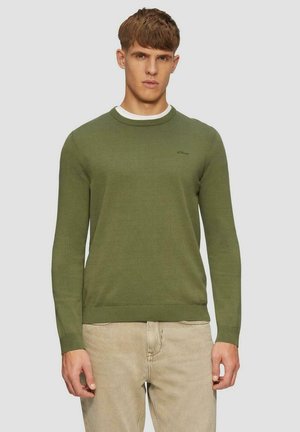 Groene gebreide trui met een ronde hals, geribbelde manchetten en zoom. Heeft een klein logo op de borst. Gepaard met lichtbeige broek.