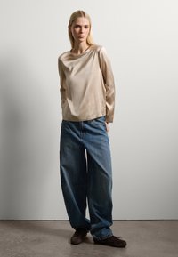 Top in seta beige con scollatura rotonda, abbinato a jeans di denim blu chiaro e morbidi. L'outfit presenta una vestibilità complessiva rilassata e una consistenza liscia.