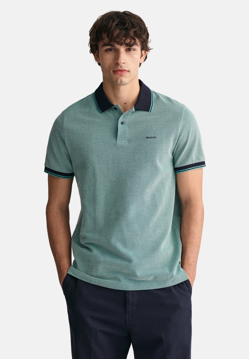 Hellgrünes Polohemd mit einem marineblauen Kragen und kontrastierenden Streifen an den Ärmeln, mit einem kleinen Logo auf der Brust und einem klassischen Schnitt.
