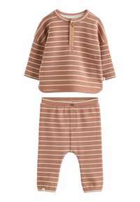 Dvojdielny outfit vyrobený z mäkkej pletenej látky. Vrchná časť je hrdzavo sfarbená s bielymi pruhmi a má zapínanie na gombíky. Nohavice majú zhodný dizajn.