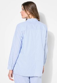 Camicia a strisce celeste con maniche lunghe, polsini abbottonati e dettagli sulla parte posteriore. Tessuto morbido, vestibilità comoda e orlo leggermente curvo.