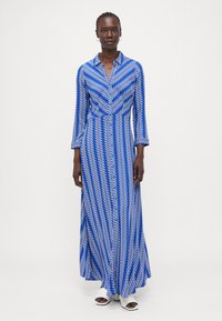 Maxikleid in Blau mit weißen Zickzackmustern, langen Ärmeln, einem Kragen und einer ausgestellten Form. Hergestellt aus leichtem Stoff für eine einfache Beweglichkeit.