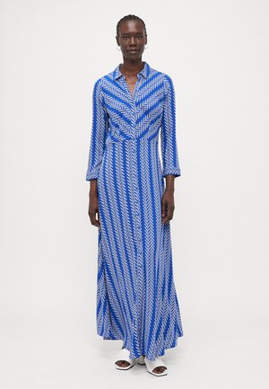 Robe maxi bleue avec des motifs en zigzag blancs, manches longues, col et forme évasée. Fabriquée en tissu léger pour faciliter le mouvement.