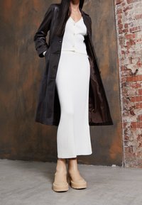 Svart lång kappa över en vit ribbad klänning och beige plattform ankle boots, som betonar en slank silhuett och strukturerade material.