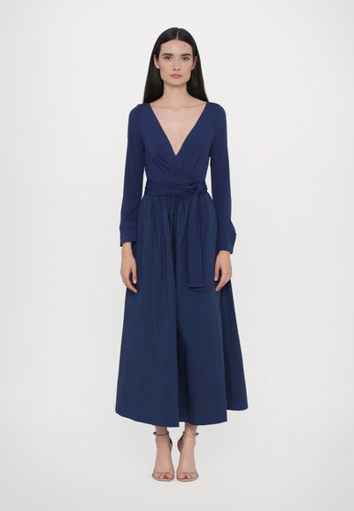 Tmavě modré zavinovací šaty s dlouhými rukávy, hlubokým výstřihem do V, páskem v pase a plnou, splývavou sukní. Hladká textura a elegantní silueta.