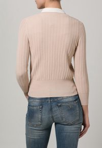 Pull en tricot côtelé rose clair avec un col blanc, des manches trois-quarts et un ourlet ajusté. Associé à un jean en denim bleu.
