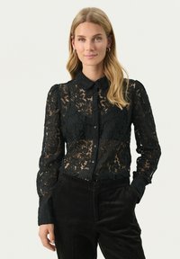Zwarte kant blouse met lange mouwen, knopenlijst aan de voorkant en een kraag. Intricate bloemmotief met doorzichtige en textuurstof.