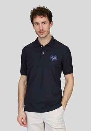 Polo shirt bleu marine en coton avec un col à deux boutons et des manches courtes. Doté d'un logo brodé circulaire sur la poitrine gauche.