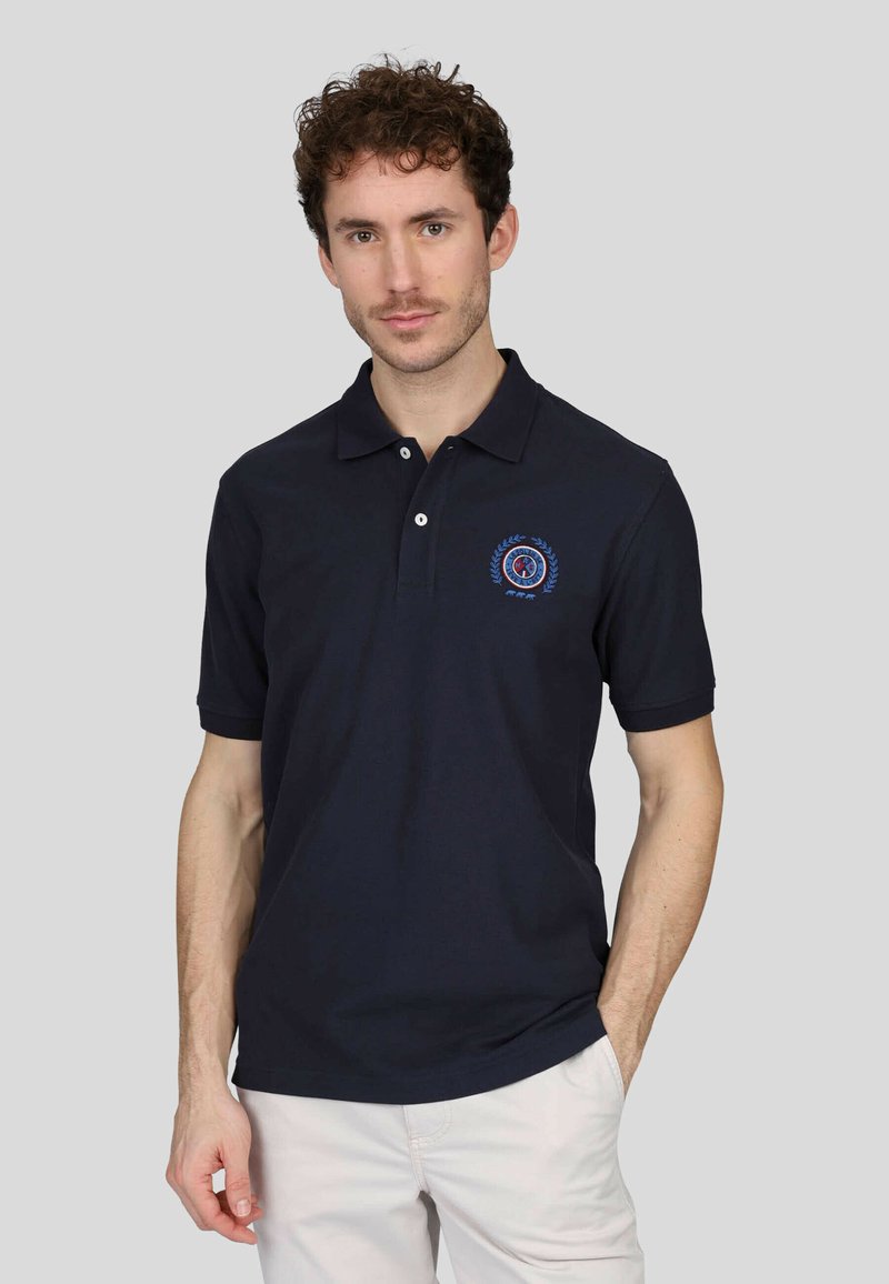 Polo shirt bleu marine en coton avec un col à deux boutons et des manches courtes. Doté d'un logo brodé circulaire sur la poitrine gauche.