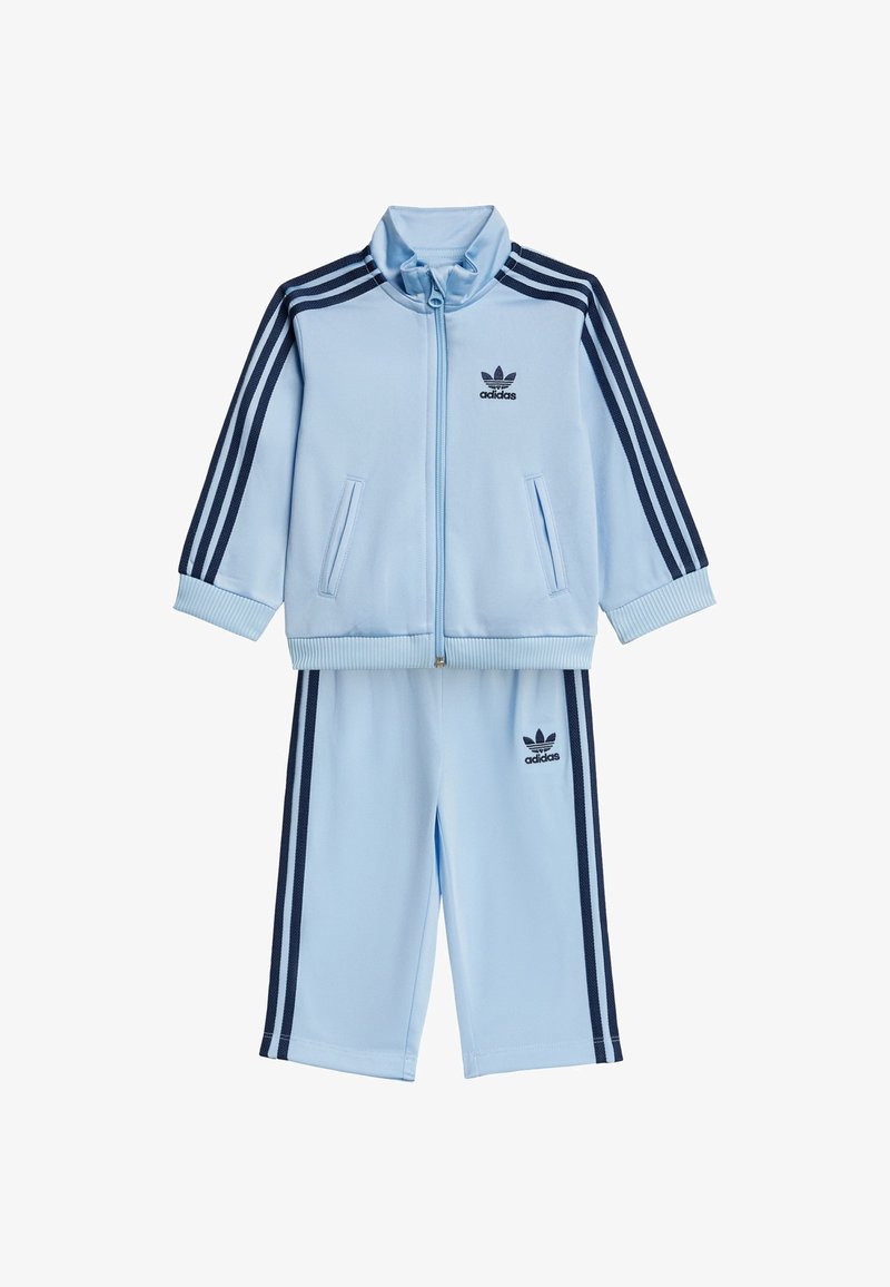 Light blue tracksuit with navy three stripes on sleeves and legs. Features zip-up jacket, ribbed cuffs, and logo on chest and pants.