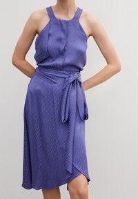 Lila klänning med en texturerad vågig mönster, halterneckband, figurnära livstycke och en knuten midjevår, med en asymmetrisk fåll.