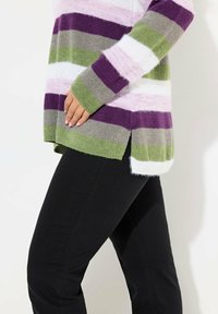 Gestreifter Strickpullover in lila, grün, pink und weiß, mit lockerer Passform, seitlichen Schlitzen und langen Ärmeln, kombiniert mit schwarzen Hosen.