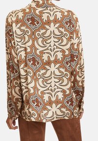 Blus med lång ärm som har en gräddfärgad botten med ett djärvt blommönster i brunt och svart. Slätt, lätt tyg med en avslappnad passform.