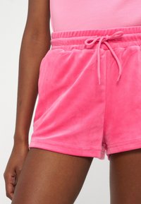 Γυναίκα που φοράει απαλό ροζ βελούδινο σορτς με ελαστική μέση και κορδόνι που δένει, συνδυασμένο με ροζ τοπ που ταιριάζει.