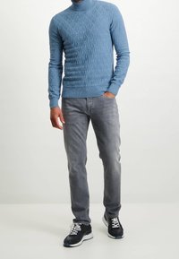 Helles blaugraues, strukturiertes Rollkragensweatshirt mit Rautenmuster, kombiniert mit grauen Jeans und dunklen Sneakers. Lässiges Outfit mit taillierter Passform.