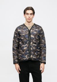 Kockás dzseki kék és bézs minták keverékével, fekete cipzárral és lekerekített nyakkivágással. Texturált, puffadt anyag.