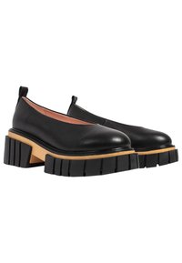 Black leather slip-on shoes with round toes, notable chunky black rubber heels, and light wooden platform detail.