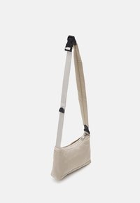 Bolso de hombro de tela beige con una sola correa ajustable, cierre de cremallera y material de correa en gris contrastante. Textura suave, diseño minimalista.