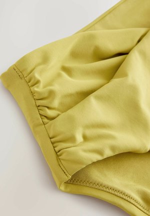 Tissu jaune clair au toucher lisse, avec des détails froncés au niveau de l'ourlet et une coupe ajustée. Pas de motifs visibles ni de matériel.