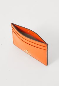 Oranž nahast kaardihoidja tekstureeritud viimistlusega, millel on mitmed kaardipesad ja kuldne kinnisosa. Siseosa on bränditud "Furla".
