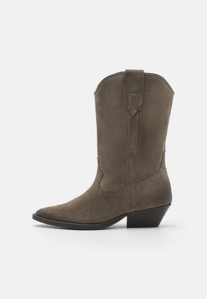 Botte Western en daim mi-mollet avec bout pointu, talon bas incliné, détails cousus et languette de traction sur le côté, de couleur taupe.