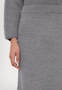 Strikket grå sweater med ribbet tekstur, brede ærmer og en tætsiddende talje. Fremhævet med en kontraststing langs manchetten.