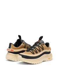 Paire de chaussures de randonnée beige et noires avec semelles épaisses, lacets noirs à motifs et marquage orange sur le talon et la languette, sur fond blanc.