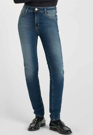 Jean slim en denim bleu foncé avec une texture lisse, comportant un bouton et une fermeture éclair, des poches avant et des coutures décoratives le long des coutures.