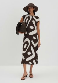 Braunes gemustertes Kleid mit weißen abstrahierten Designs, kürzeren Ärmeln und geradem Schnitt. Die Accessoires umfassen einen geflochtenen braunen Hut und eine Tasche.