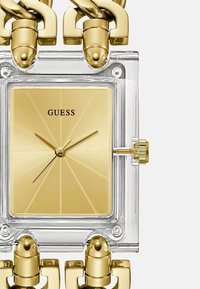 Rektangulær klar ur med en gulddial med solstrålmønster, guld time- og minutthænder samt guld kædelænkearmbånd.