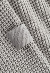 Grauer Strickstoff mit einem eingewebten rechteckigen Etikett, auf dem "JOOP! JEANS" steht, das auf dem Material genäht ist.