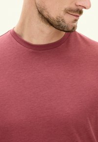 T-shirt a maniche corte con collo a girocollo in tessuto bordeaux testurizzato. Presenta una finitura liscia e un collo a coste.
