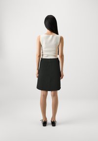 Haut sans manches blanc à côtes associé à une jupe noire au genou, porté avec des chaussures noires. Texture lisse, design simple, silhouette ajustée.
