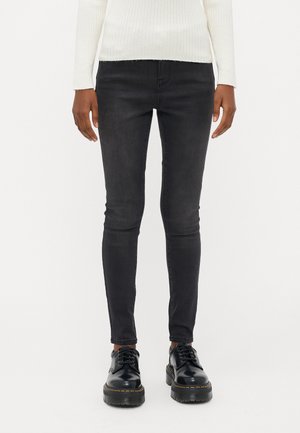 Black skinny jeans with a smooth texture, featuring a classic five-pocket design. Paired with black lace-up shoes and a white ribbed sweater.