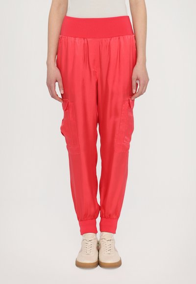 Pantalones cargo de satén rojo con una cintura acanalada, puños elásticos y dos bolsillos laterales. Textura suave y un ajuste relajado. Combinados con zapatillas beige.