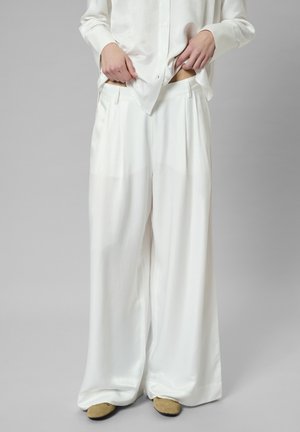 White wide-leg trousers made of smooth fabric with a high waist, featuring pleats and side pockets. Worn with a matching button-up shirt.