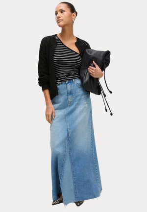 Jupe maxi en denim à coupe droite, délavage bleu clair et détail de couture sur le devant. Associée à un cardigan noir texturé et un haut rayé.