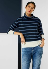 Marineblauer gestreifter Pullover mit einem Schalkragen und hellgrauem Saum, kombiniert mit blauen Jeans. Weicher Stoff mit lässiger Passform.