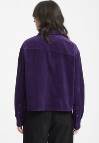 Lila kordflöjelsskjorta med långa ärmar, knäppte manschetter och en kortad design. Texturerat tyg med vertikala ränder.