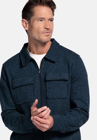 Marineblauwe zip-up jas van een gestructureerde stof, met een kraag en twee voorzakken. Gladde binnenvoering, casual pasvorm.