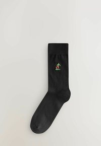 Calzino di cotone nero con orlo a costine; presenta una piccola figura ricamata che calcia un pallone da calcio nei colori verde, rosso e bianco.