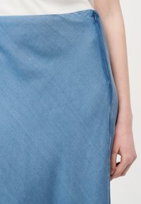 Κλείσιμο πλάνου ενός ατόμου που φοράει φουστάνι από ανοιχτό μπλε τζιν με φερμουάρ στο πλάι και άσπρο μπλουζάκι κρυμμένο μέσα.