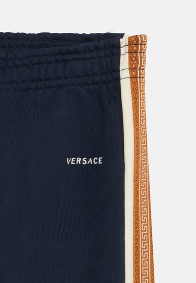 Σκούρο μπλε παντελόνια Versace με ελαστική μέση, με λευκή και καφέ σχεδιασμένη πλευρική ρίγα.