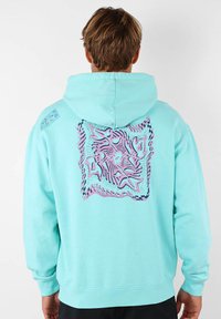 Hoodie vert menthe arborant un grand motif abstrait rose et bleu au dos, avec une coupe décontractée et une capuche à cordon.