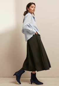 Chemise bleu clair à manches longues portée avec une jupe midi noire et des bottines en daim bleu marine. La jupe a un design fluide avec une texture lisse.