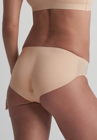 Beige naadloze hipster onderwear met een gladde textuur, lage taille, en subtiele stiksels bij de tailleband en beenopeningen.
