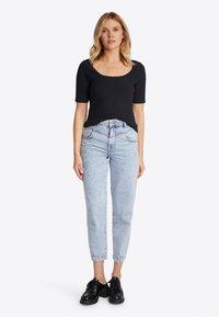 Top nero a maniche corte a coste abbinato a pantaloni in denim chiaro a vita alta e scarpe nere con lacci. Design semplice e aderente con scollatura arrotondata.