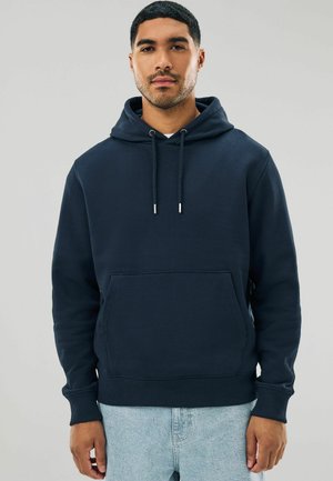 Marineblauwe hoodie gemaakt van zachte stof, met een kangoeroezak, een capuchon met koord en ribgebreide manchetten en zoom. Gepaard met lichtblauwe jeans.